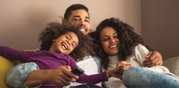 Family of three watching cartoons on the couch at home